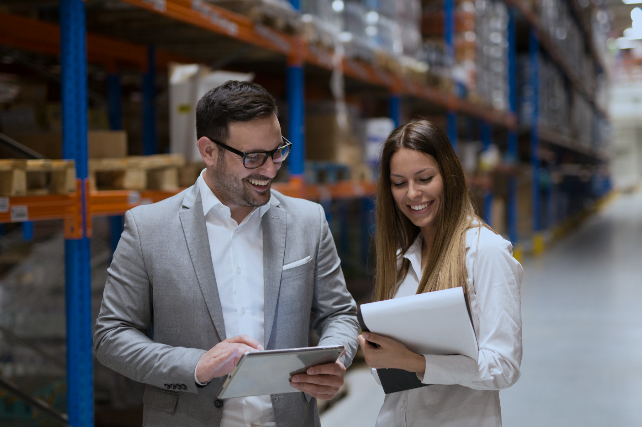 Um homem e uma mulher dentro de um armazém de fulfillment conversando e fazendo anotações em folhas de papel